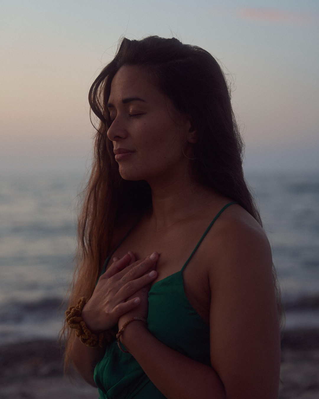 Woman standing by the ocean at sunset with her hand over her heart